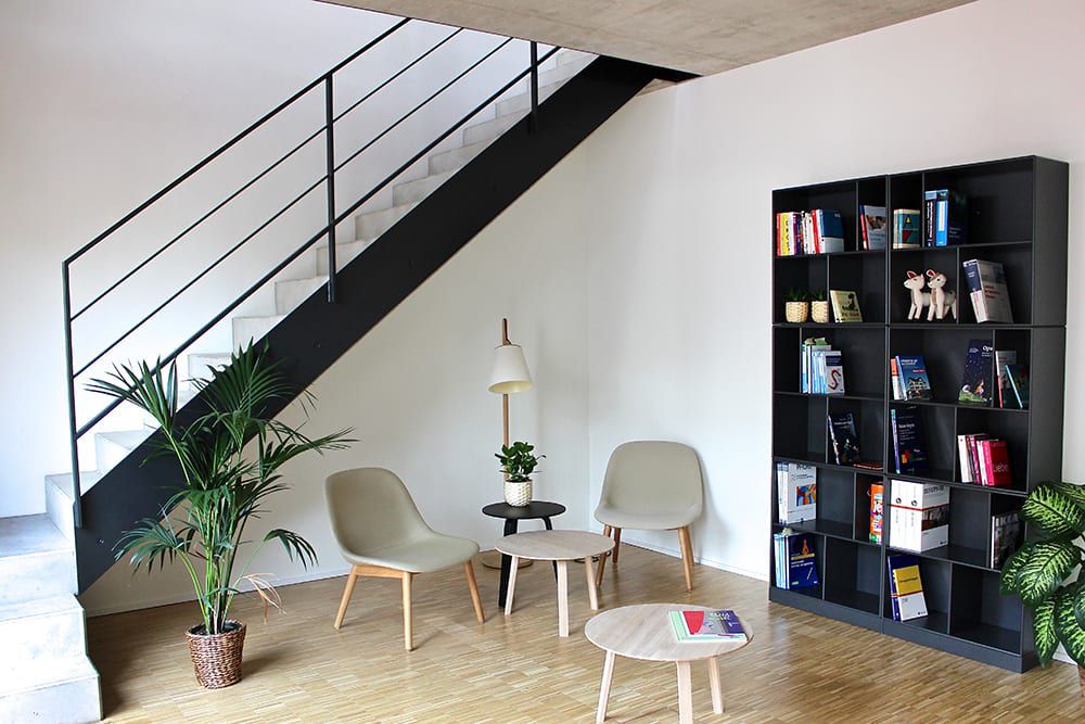 Ein Raum mit einer Treppe und zwei grauen Stühlen, einem Bücherregal und einem Tisch.